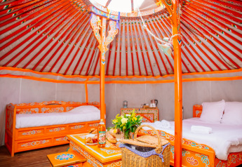 Bunte, traditionell eingerichtete Jurte mit Betten und Tisch in Domaine EcÔtelia, Frankreich, Glamping-Stil.