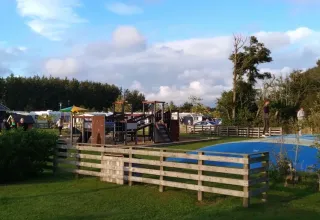 Spielplatz und Hüpfkissen bei Tornby Strand Camping in Nordjütland, mit Bäumen und blauem Himmel.