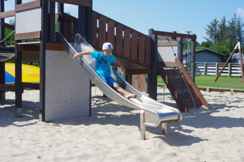 Un bambino con maglietta blu e cappellino scende da uno scivolo in metallo nell’area giochi di Tornby Strand Camping, Danimarca.