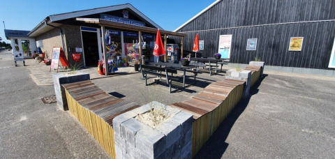 Udendørs område ved Tornby Strand Camping i Nordjylland med bænke, flag og butik i baggrunden.