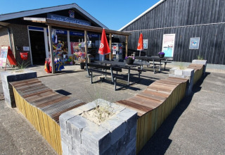 Udendørs område ved Tornby Strand Camping i Nordjylland med bænke, flag og butik i baggrunden.