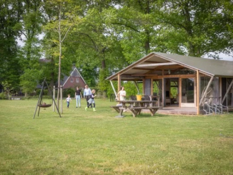 Famiglia si gode il tempo all’aperto davanti a una baita al Landrijk de Reesprong, parco vacanze in Overijssel.