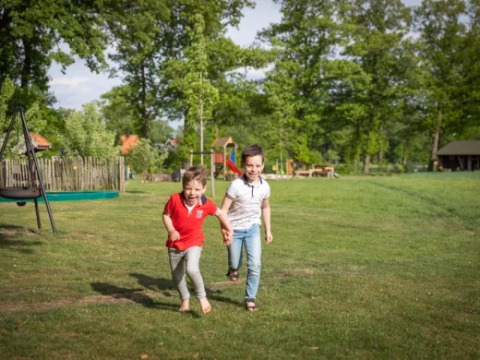 Zwei Kinder rennen lachend über eine Wiese im Landrijk de Reesprong, einem Ferienpark in Overijssel, Niederlande.