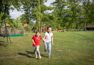 Due bambini sorridenti corrono sull'erba a Landrijk de Reesprong, un parco vacanze in Overijssel, Paesi Bassi.
