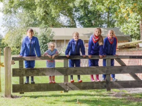 Kinder in blauen Overalls stehen auf einem Holztor im Landrijk de Reesprong Ferienpark in Overijssel.