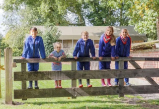 Kinder in blauen Overalls stehen auf einem Holztor im Landrijk de Reesprong Ferienpark in Overijssel.