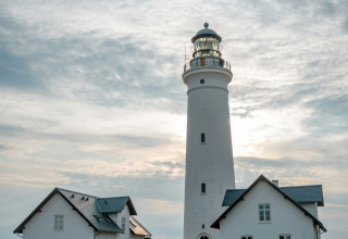 Faro e case bianche sotto un cielo nuvoloso vicino a Hirtshals, Jutland settentrionale, Danimarca.