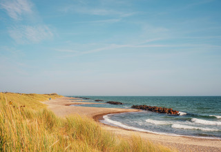 Kystlandskab ved Tornby Strand Camping i Nordjylland, Danmark, med sandstrand og bølger under blå himmel.