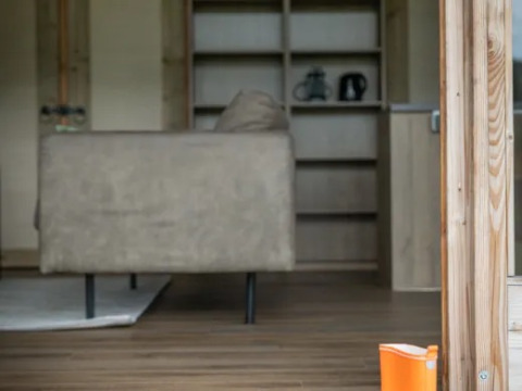 Innenansicht der Wellness Luxe Lodge bei Landrijk de Reesprong mit Sofa, Holzboden und orangen Gummistiefeln.