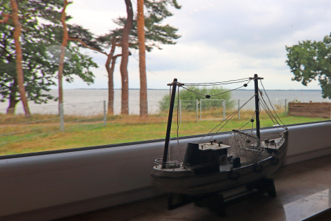 Modelschip op vensterbank met uitzicht op strand en bomen bij lodge Am Strand in Duitsland.