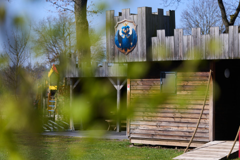 Houten lodge van Kasteel Uylenburght bij Camping de Zandstuve, Nederland, gezien door groen lentegebladerte.