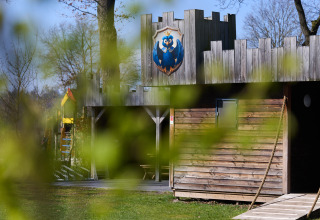 Cabaña de madera en Kasteel Uylenburght del camping de Zandstuve, Países Bajos, vista entre hojas verdes.