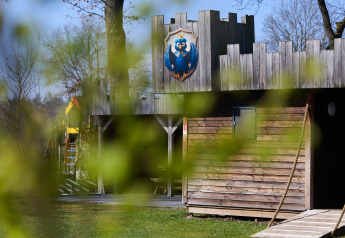 Holzlodge Kasteel Uylenburght im Camping de Zandstuve, Niederlande, mit grünen Blättern im Vordergrund.