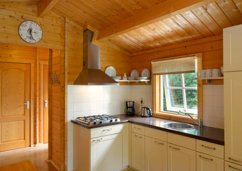Kitchen in a chalet at Campsite Mareveld in the Netherlands with wood decor, window, dishes, and stove.