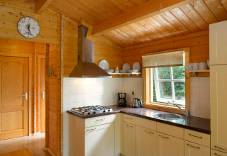 Kitchen in a chalet at Campsite Mareveld in the Netherlands with wood decor, window, dishes, and stove.