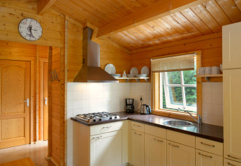 Keuken in chalet op Camping Mareveld in Nederland met houten interieur, raam, servies en fornuis.