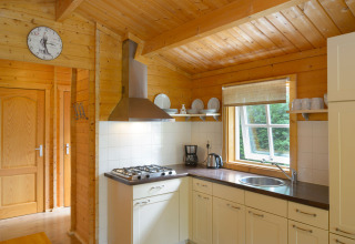 Cucina in uno chalet al campeggio Mareveld nei Paesi Bassi, con legno, finestra, piatti e fornelli.