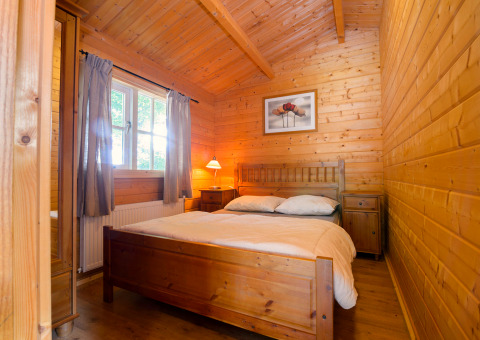 Wood-paneled bedroom with double bed, window and bedside lamps at Chalet, Campsite Mareveld, Netherlands.