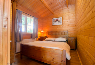 Wood-paneled bedroom with double bed, window and bedside lamps at Chalet, Campsite Mareveld, Netherlands.