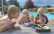 Trois enfants assis près d'une table au bord d'une piscine à Park Drentheland, Drenthe, Pays-Bas, avec des pommes.