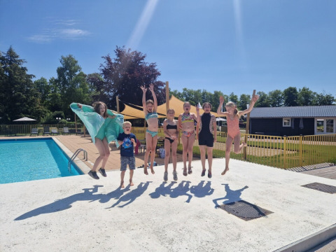 Kinderen springen samen bij een zwembad in de zon op Park Drentheland, Drenthe, Nederland.