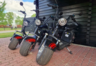 Drie elektrische scooters bij een zwart schuurtje in Park Drentheland, een vakantiepark in Drenthe, Nederland.