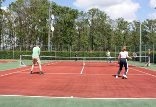 Vier mensen spelen tennis op een buitenbaan in Park Drentheland, omringd door bomen en hekwerk.