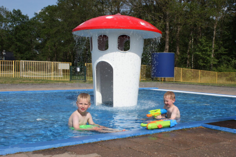 Twee kinderen spelen met waterpistolen in een kinderbad met paddenstoelfontein in Park Drentheland.