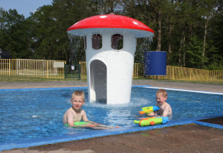 Twee kinderen spelen met waterpistolen in een kinderbad met paddenstoelfontein in Park Drentheland.