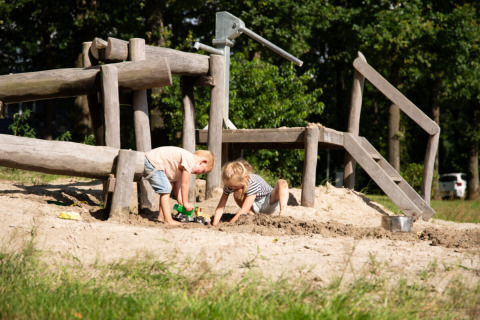 Twee kinderen spelen in het zand bij een houten speeltuin in Park Drentheland, Drenthe, Nederland.