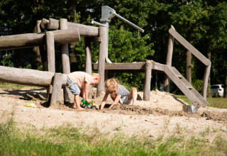 Twee kinderen spelen in het zand bij een houten speeltuin in Park Drentheland, Drenthe, Nederland.