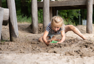 Een kind speelt in de modder onder een houten constructie in Park Drentheland, Drenthe, Nederland.
