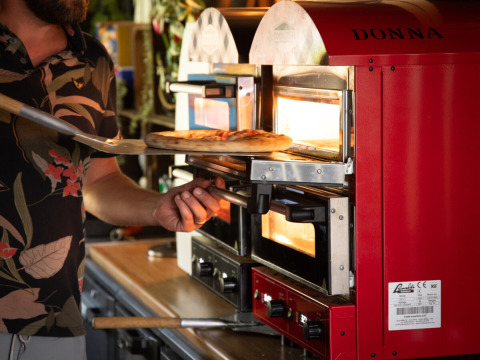 Man bakt pizza in een rode oven met 'DONNA' bij Park Drentheland, vakantiepark in Drenthe, Nederland.