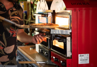 Man bakt pizza in een rode oven met 'DONNA' bij Park Drentheland, vakantiepark in Drenthe, Nederland.
