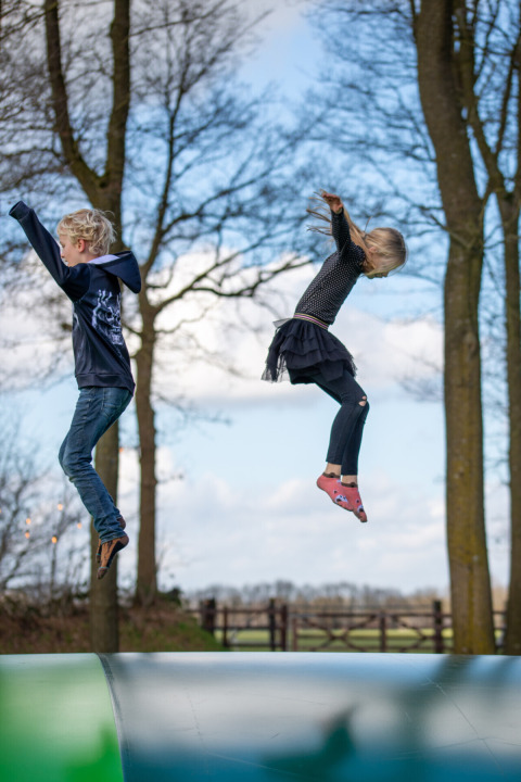 Twee kinderen springen op een luchtkussen bij Park Drentheland in Drenthe, Nederland, omringd door bomen.