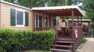 Cabaña SunLodge Redwood con porche de madera cubierto, zona de comedor exterior y vegetación al lado.