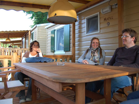 Trois personnes se détendent autour d’une table en bois devant un SunLodge Maple à Altomincio Family Park, Italie.