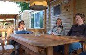 Tres personas se relajan en una mesa de madera frente a una cabaña SunLodge Maple en Altomincio Family Park, Italia.