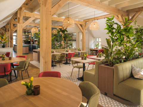 Bright, modern restaurant at glamping site with wooden beams, plants, and colorful seating arrangements.