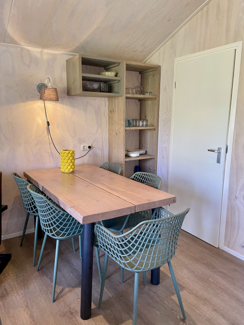 Dining area in a safari lodge at Campsite de Noetselerberg, featuring a wooden table and six green chairs.
