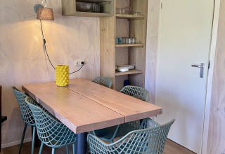Coin repas d'une tente safari au camping de Noetselerberg, table en bois et six chaises vertes modernes.