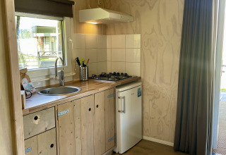 Compact kitchenette with wooden cabinets, gas stove, and mini fridge in a safari lodge at Campsite de Noetselerberg.