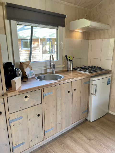 Modern kitchenette in a safari lodge at Campsite de Noetselerberg, Netherlands, with wooden cabinets and stove.