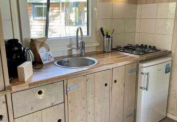 Modern kitchenette in a safari lodge at Campsite de Noetselerberg, Netherlands, with wooden cabinets and stove.