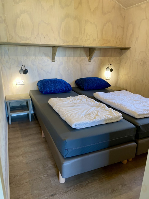 Bedroom in a Safari lodge tent at Campsite de Noetselerberg featuring two single beds and blue pillows.