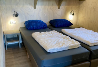 Chambre d'une tente Safari lodge au Camping de Noetselerberg avec deux lits simples et oreillers bleus.