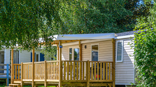 Außenansicht eines Mobile Home Premium mit Holzterrasse und viel Grün an einem sonnigen Tag.