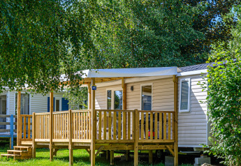Vista exterior de Mobile home Premium con porche de madera rodeado de árboles y vegetación al sol.