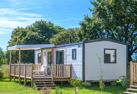 Casa mobile Premium con terrazza in legno e lettini prendisole, immersa nel verde e tra gli alberi.