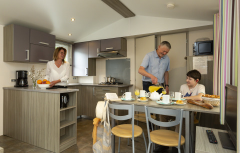 Family enjoys breakfast together inside a modern mobile home at Flower Camping Le Kerleyou in France.